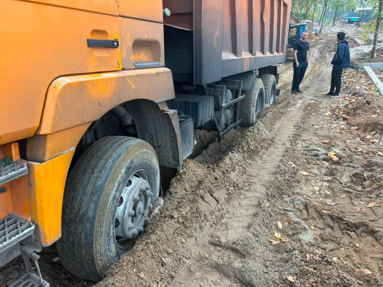 фура застряла в грязи на грунтовом подъезде, рядом стоят два человека